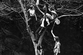 A black and white photo circa 1970s with students in period clothing climbing an enormous tree.